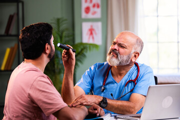 Senior Indian physician uses medical torch to examine young male patient in modern clinic