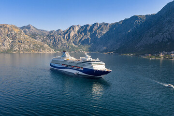 drone shot of a luxury ocean liner at anchor in a serene sea bay with a breathtaking mountain backdrop, symbolizing high-end vacation and global tourism