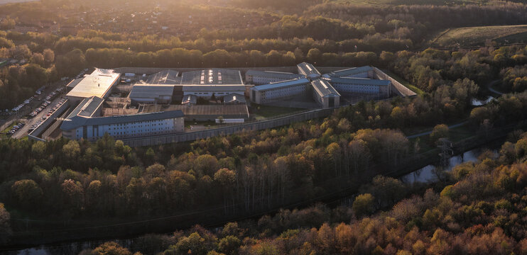 A high-angle aerial view of HMP Forest Bank prison in Salford, showcasing its distinctive radial architecture and security perimeter at sunset.