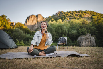 Young woman with headphones sit on the blanket listen music and sing