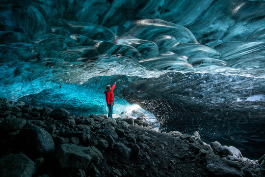 View of a person in a red jacket stands in awe beneath the sapphire ice cave, a symphony of textures and colors, Vatnajokull glacier, Breidamerkurjokull glacier, Iceland.