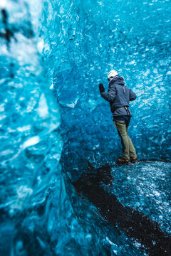 View of a lone explorer touches the icy blue sapphire cavern walls, a stark contrast to the dark crevice below, Vatnajokull glacier, Iceland.