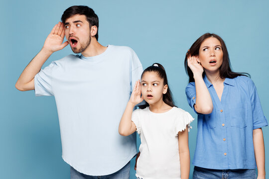 Young curious nosy shocked parents mom dad with child kid daughter girl wear casual clothes try to hear you overhear listening intently isolated on plain blue background Family day parenthood concept