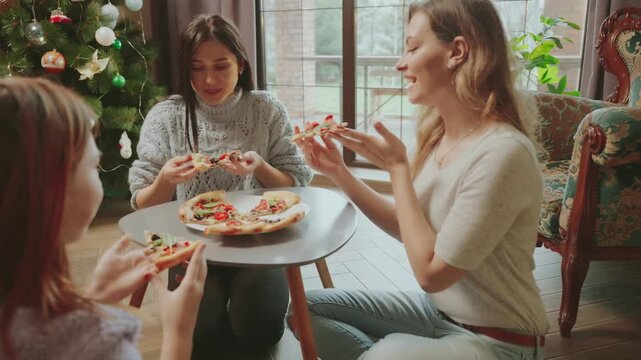 happy young people eating pizza at home, smiling face cheerful female group enjoying food meal dining sitting together at floor, hungry girls family friends sharing lunch at meeting. cozy living room