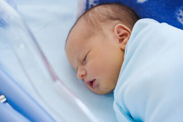 Newborn baby resting in hospital bed in blue attire