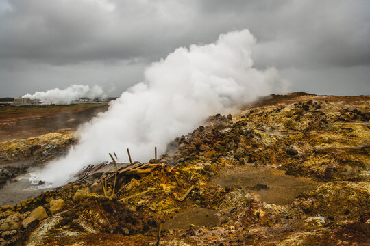 View of geothermal steam rising from the ochre-stained earth and rugged rocks under a brooding sky, an ethereal scene in Hveragerdi Geothermal Park, Keflavik, Iceland.