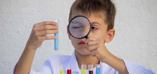 Little boy in lab coat conducting chemical experiments with test tubes and microscope