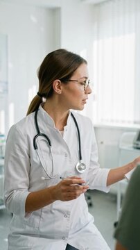 Female doctor in white coat writing notes on a clipboard during a medical consultation. Professional physician talking to a patient in a bright clinic. Healthcare and medicine concept