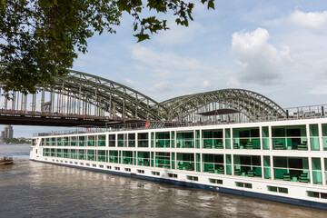 A large modern river cruise ship on the Rhine river with the iconic Hohenzollern Bridge in the background in Cologne