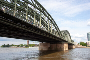 Low angle view of the massive steel arches of the Hohenzollern Bridge spanning the Rhine river with pedestrians walking across in Cologne