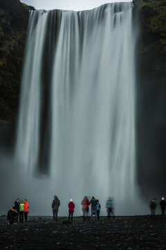View of the majestic Skogafoss waterfall cascading down rugged cliffs, with tiny figures of visitors adding scale to the scene, Skogar, South Iceland, Iceland.
