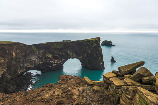 View of dramatic cliffs meet the turquoise sea under a moody sky, with the iconic Dyrholaey arch standing majestically in Vik, South Island, Iceland.