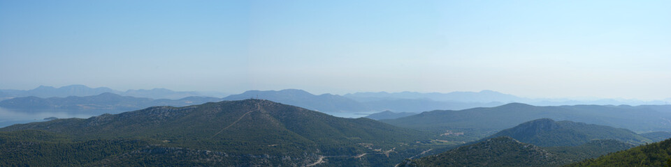 Naklejka premium A wide panoramic landscape view from the Sveti Ivan peak on Peljesac peninsula looking southeast over lush green hills and distant mountain ranges under a clear sky