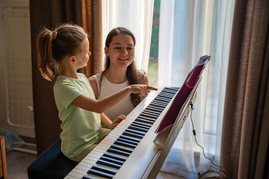 Young girl learning piano with teacher during private music lesson at home. Individual piano education, child development, and focused learning process.