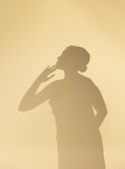 Soft silhouette of a woman clapping hands against a warm beige background, creating a minimalist and artistic shadow composition with calm and emotional atmosphere.