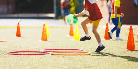 Children in Training with Football Equipment. Kid Jumping Over Obstacles. Football Speed Training. Young Footballer in Sportswear at Training Session on Grass Soccer Field