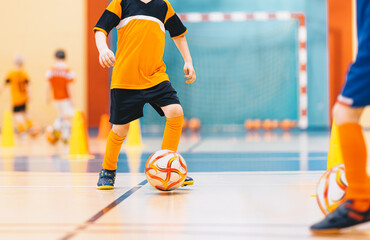 Football training for children. Indoor soccer young player with a soccer ball in a sports hall. Sport background.