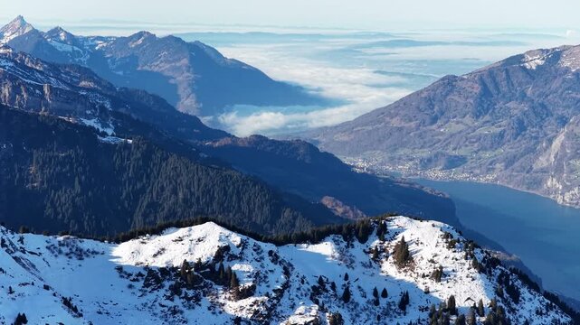 Aerial view of the Churfirsten mountains overlooking Walensee lake in Switzerland. Snowy alpine slopes and deep blue water create a dramatic landscape, a concept of scale, nature, and perspective.