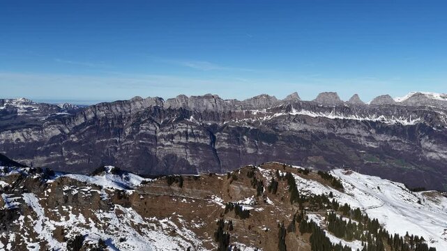 Aerial view of the Churfirsten mountain range from Flumserberg in Switzerland. Snow-covered alpine peaks and rocky ridges under clear blue sky, concept of freedom, nature and adventure.