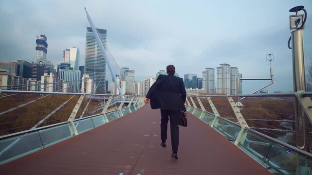 Excited Caucasian businessman celebrates success with heel-click jump turn and fist pumps on Saetgang Munhwa Bridge overlooking Yeouido skyscrapers in Seoul