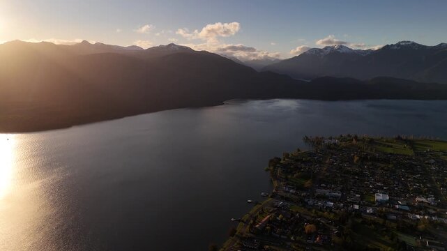 4K60 Aerial View of Te Anau Town, Lake, and Mountains in New Zealand - Sunset with Sunflare
