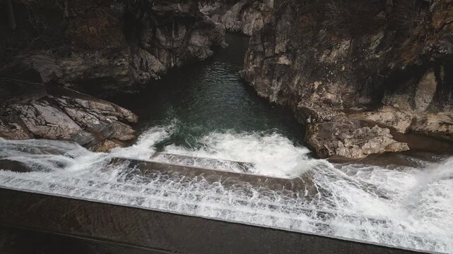 Drone surges forward into Lechfall gorge at Fussen, plunging toward foaming turquoise pool amid massive dam overflow and sheer rocky walls. Intense Bavarian cascade.