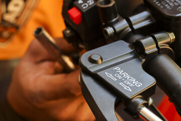 Close up view showing focused maintenance check motorcycle handlebar parking brake lever mechanism featuring clear white lettering with mechanic hand blurred warm orange background working