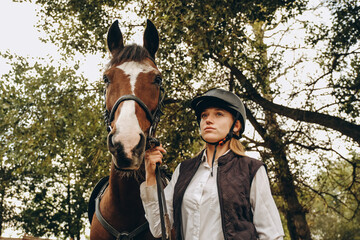 A young female equestrian stands near her horse and prepares for a competition.