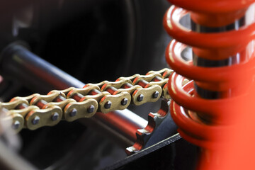 Closeup of motorcycle drive chain and bright orange suspension spring showing mechanical power and industrial precision engineering on high performance vehicle part