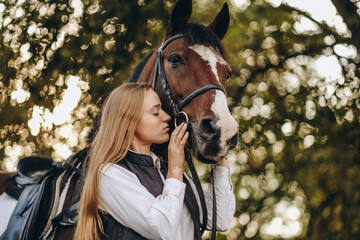 A young female equestrian stands near her horse and prepares for a competition.