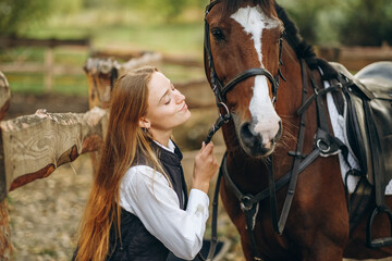 Obraz premium A young female equestrian stands near her horse and prepares for a competition.
