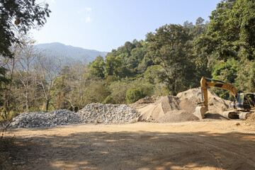 Peaceful nature landscape with construction site having excavator working near pile of gravel stone under blue sky feeling busy but calm amidst green mountain forest environment © CoreRock