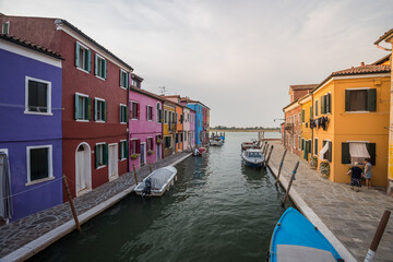 Colorful canal street on Burano island near Venice with vibrant traditional houses, small boats, calm waterway, and authentic Italian lagoon atmosphere under soft evening light