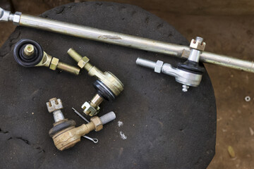 Steering rack tie rod end part lying on dark dirty surface at car garage for repair and replacement show shiny metal detail waiting for mechanic work to fix vehicle suspension system problem