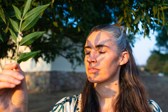 Woman holding green leaf with sunlight shadow on face