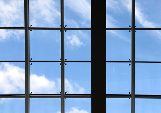 Upward view of a modern glass roof with metal framing against a blue sky with soft clouds. Clean