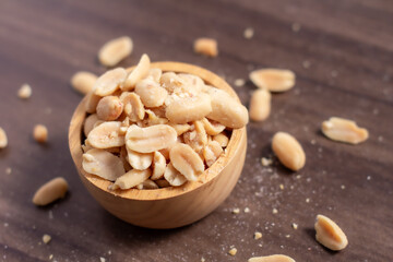 Peanuts in a wooden cup rest on a natural wood floor, creating a warm and rustic food-themed scene.