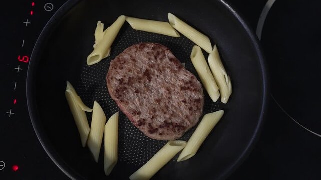 Cuisson d'un steak hach&eacute; dans une po&ecirc;le sur une plaque de cuisson en c&eacute;ramique.