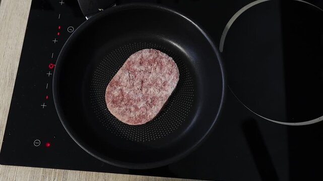 Cuisson d'un steak hach&eacute; dans une po&ecirc;le sur une plaque de cuisson en c&eacute;ramique.