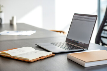 laptop on a table with an open book and a closed notebook