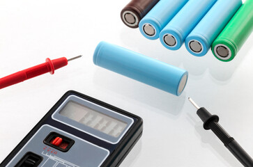 Close-up of a voltmeter measuring voltage on 18650 lithium-ion battery cells, isolated on white background.