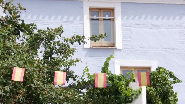 Pale blue facade in Molv&iacute;zar, Granada, with wooden windows and a garland of Spanish flags. Festive rural atmosphere in a white village of Andalusia.