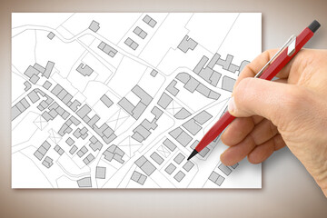 Hand drawing an imaginary cadastral map of territory with buildings, fields, roads and land parcel above a desk - concept image