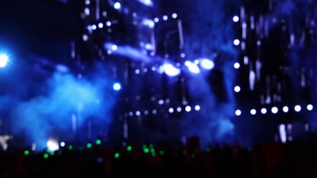 Blurry view of people dancing on the dance floor during a concert show at a festival. Crowd enjoying loud music at live dj set with laser lights, fire show, smoke effects. Night club event in bokeh.