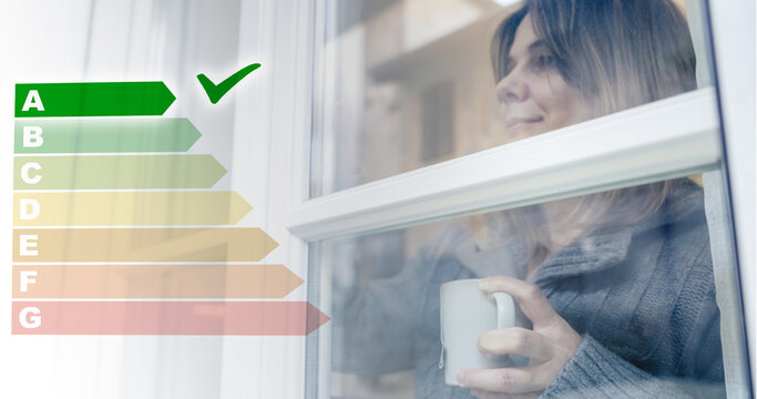 Relaxed woman with a warm mug looks through an energy efficient window featuring an overlaid energy rating scale, high thermal insulation and eco friendly home improvements for saving money