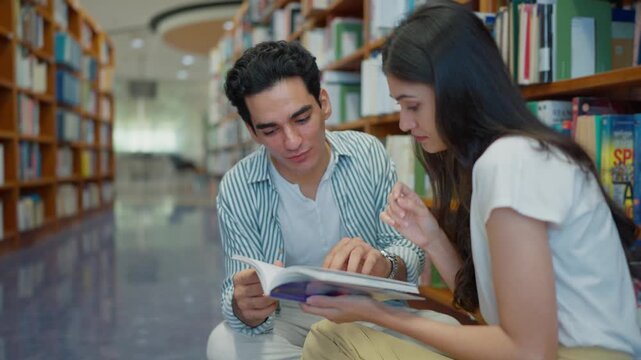 Two multi-ethnic university students sitting next to bookshelves, searching for information in books at a university library, exchange student program concept