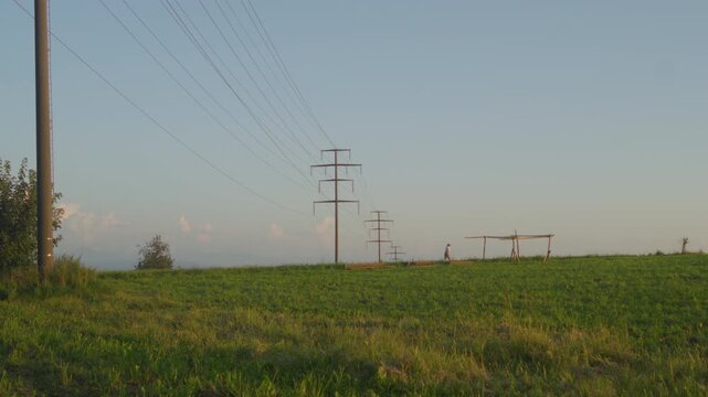 Woman walking on a footpath with power poles on a summer day, Switzerland