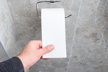 A man takes white toilet paper in his hand. Close-up of a residential building restroom, bathroom.