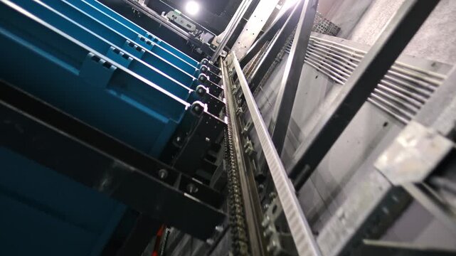 A detailed close-up view of a chain-driven lift mechanism inside an automated robotic parking system, showing metal structures, moving components, and a vehicle positioned on the platform.