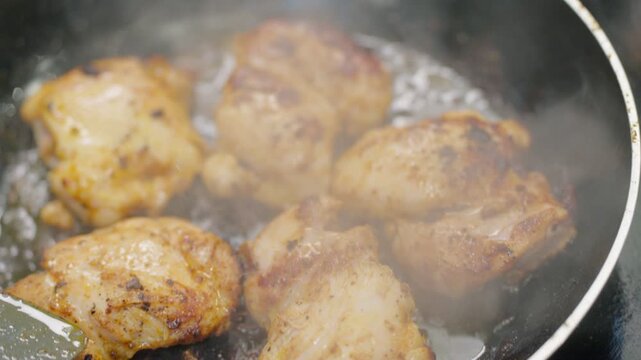 Close up shot of marinated chicken thighs cooking at high heat in a pan with bubbling oil and steam